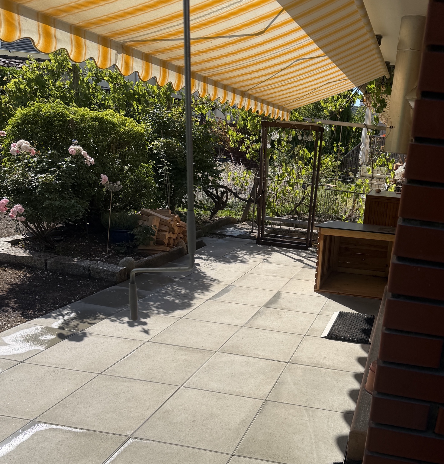 Gartensitzplatz mit hellen Platten unter einer Markise